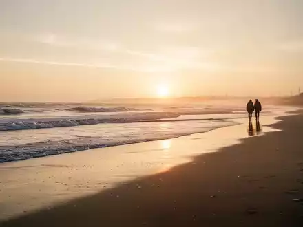 Ein ruhiger Strand bei Sonnenuntergang in der Nebensaison mit einem Paar in der Ferne, das die Ruhe genießt. - Foto: über boerse-global.de
