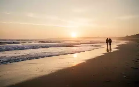 Ein ruhiger Strand bei Sonnenuntergang in der Nebensaison mit einem Paar in der Ferne, das die Ruhe genießt. - Foto: über boerse-global.de