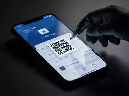 Ein Smartphone mit einer mobilen Geldbörse auf dem Bildschirm, überlagert von einer Schattenhand, die einen QR-Code einfügt. - Foto: über boerse-global.de