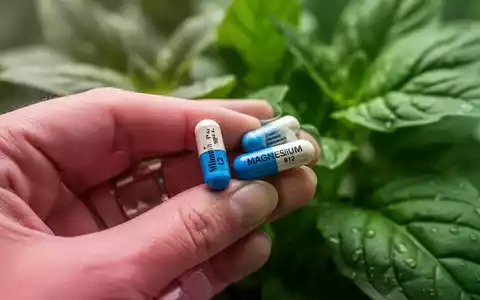 Eine Hand hält zwei verschiedene Kapseln, die Vitamin B12 und Magnesium darstellen, vor einem unscharfen grünen Hintergrund. - Foto: über boerse-global.de