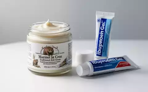 Ein Tiegel Murmeltierfett-Creme neben einer Tube Ibuprofen-Gel auf einer weißen Oberfläche, die den Kontrast zwischen Natur- und Synthetikprodukten darstellt. - Foto: über boerse-global.de