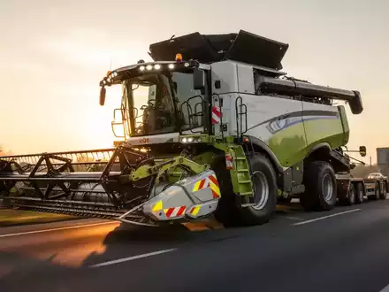Ein großer Mähdrescher mit abgenommenem Schneidwerk wird auf einer öffentlichen Straße transportiert, mit Fokus auf die Verkehrssicherheit. - Foto: über boerse-global.de