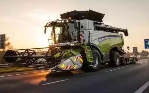 Ein großer Mähdrescher mit abgenommenem Schneidwerk wird auf einer öffentlichen Straße transportiert, mit Fokus auf die Verkehrssicherheit. - Foto: über boerse-global.de