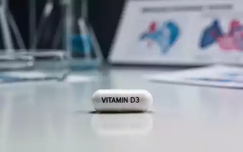 Eine einzelne weiße Vitamin D3 Kapsel liegt auf einer sauberen Oberfläche, im Hintergrund verschwommen Laborgeräte. - Foto: über boerse-global.de