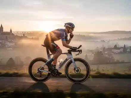 Eine verschwommene Aufnahme eines einzelnen Ultra-Radfahrers, der bei Sonnenaufgang durch eine malerische europäische Landschaft fährt. - Foto: über boerse-global.de