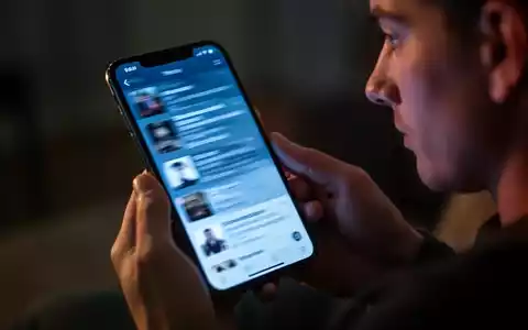 Eine Nahaufnahme eines Smartphones, das in Händen gehalten wird, der Bildschirm zeigt einen schnell scrollenden Feed in einem abgedunkelten Raum. - Foto: über boerse-global.de