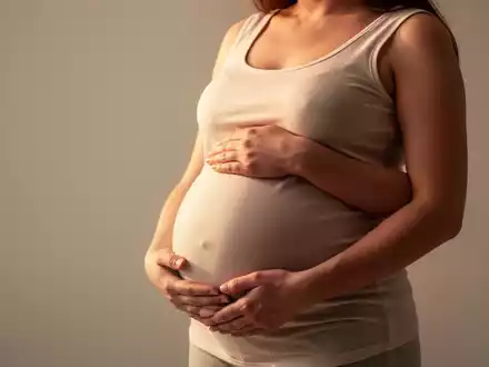 Eine schwangere Frau mit den Händen auf ihrem Bauch, umgeben von einem weichen, warmen Licht, symbolisiert Fürsorge und Gesundheit. - Foto: über boerse-global.de