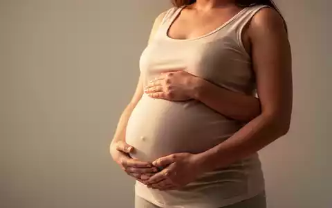 Eine schwangere Frau mit den Händen auf ihrem Bauch, umgeben von einem weichen, warmen Licht, symbolisiert Fürsorge und Gesundheit. - Foto: über boerse-global.de