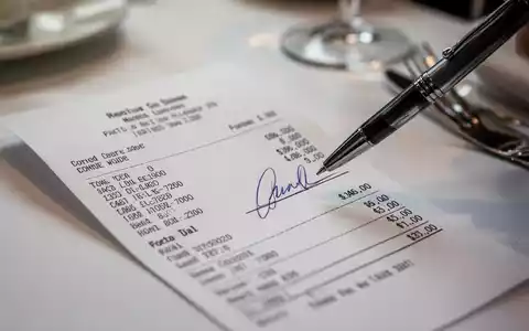 Nahaufnahme einer Restaurantrechnung mit einem Stift, der zum Unterzeichnen bereitliegt, vor verschwommenem Hintergrund eines Geschäftsessens. - Foto: über boerse-global.de