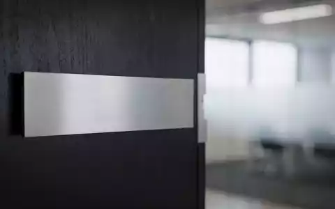 Nahaufnahme einer modernen Namenstafel oder Bürotür in einer professionellen Büroumgebung, die neue Führung andeutet. - Foto: über boerse-global.de