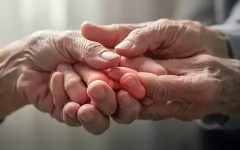 Nahaufnahme einer Hand, die sanft die Fingerknöchel der anderen Hand berührt, was auf Fingergelenkarthrose hindeutet. - Foto: über boerse-global.de