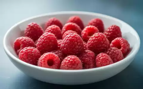 Nahaufnahme von frischen, leuchtend roten Himbeeren, die sorgfältig in einer flachen, weißen Keramikschale angeordnet sind. - Foto: über boerse-global.de
