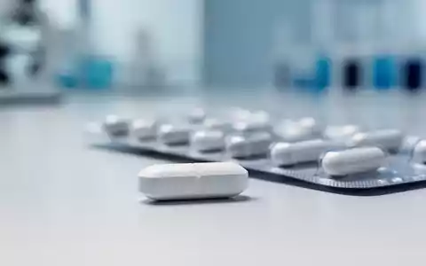 Eine einzelne weiße Pille liegt auf einer sauberen Oberfläche, im Hintergrund eine verschwommene Medikamentenpackung, die pharmazeutische Innovation symbolisiert. - Foto: über boerse-global.de