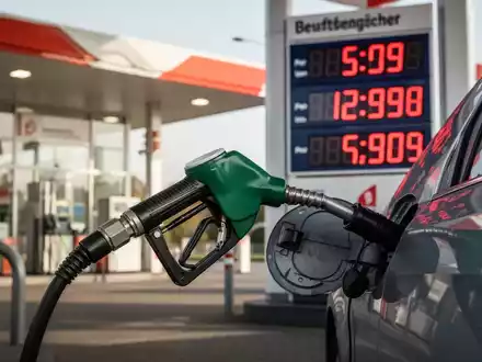 Eine Zapfpistole füllt Benzin in ein Auto, im Hintergrund eine Tankstelle mit einer digitalen Preisanzeige, die hohe Kraftstoffkosten anzeigt. - Foto: über boerse-global.de