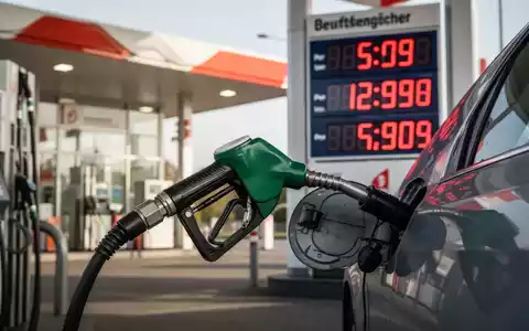 Eine Zapfpistole füllt Benzin in ein Auto, im Hintergrund eine Tankstelle mit einer digitalen Preisanzeige, die hohe Kraftstoffkosten anzeigt. - Foto: über boerse-global.de