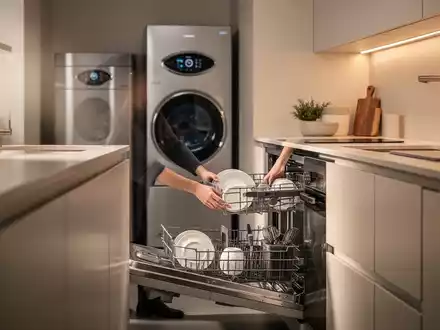 Eine moderne, energieeffiziente Küche mit einem Wärmepumpentrockner und einer Person, die eine Spülmaschine belädt. - Foto: über boerse-global.de