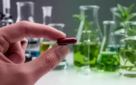 Eine Hand hält eine rote Berberin-Kapsel über einem unscharfen Hintergrund mit Laborgeräten und Pflanzenextrakten. - Foto: über boerse-global.de