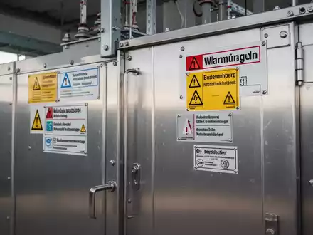 Eine moderne Trafostation mit klaren Warnschildern und Typenschildern, die die Einhaltung deutscher Sicherheitsvorschriften betonen. - Foto: über boerse-global.de