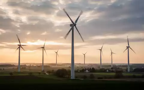 Ein Windpark in einer ländlichen deutschen Landschaft bei Sonnenaufgang oder Sonnenuntergang, mit modernen Windturbinen vor einem dramatischen Himmel. - Foto: über boerse-global.de