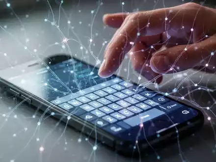 Ein Smartphone mit virtueller Tastatur, abstrakten KI-Linien und einer darüber gestikulierenden Hand, die neue Barrierefreiheitsfunktionen darstellt. - Foto: über boerse-global.de