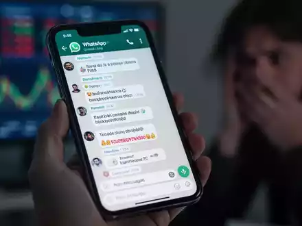 Nahaufnahme eines Smartphones mit einem verdächtigen WhatsApp-Gruppenchat, gehalten von einer Person, die Sorge ausdrückt. - Foto: über boerse-global.de