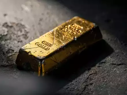 Ein leicht angelaufener Goldbarren ruht auf einer dunklen, strukturierten Oberfläche und spiegelt einen subtilen Abwärtstrend wider. - Foto: über boerse-global.de