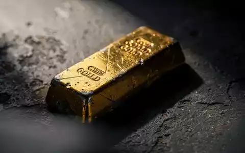 Ein leicht angelaufener Goldbarren ruht auf einer dunklen, strukturierten Oberfläche und spiegelt einen subtilen Abwärtstrend wider. - Foto: über boerse-global.de