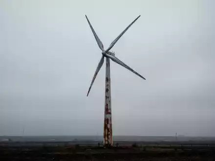 Eine stillstehende Windturbine unter einem bewölkten Himmel, umgeben von karger Landschaft, die mangelnde Impulse im Bereich sauberer Energie symbolisiert. - Foto: über boerse-global.de