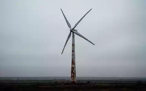 Eine stillstehende Windturbine unter einem bewölkten Himmel, umgeben von karger Landschaft, die mangelnde Impulse im Bereich sauberer Energie symbolisiert. - Foto: über boerse-global.de