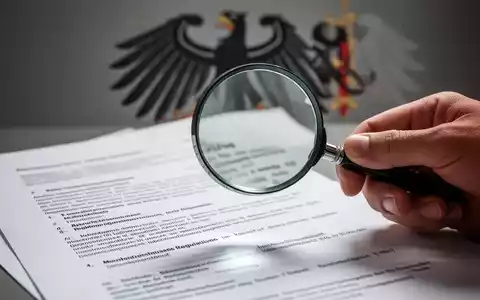 Eine Hand hält eine Lupe über ein Dokument, das Tarifverträge symbolisiert, im Hintergrund verschwommen ein Bundesadler. - Foto: über boerse-global.de
