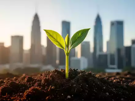 Ein grüner Trieb bricht durch dunkle Erde, im Hintergrund eine verschwommene Skyline eines Finanzviertels. Symbolisiert nachhaltiges Wachstum. - Foto: über boerse-global.de