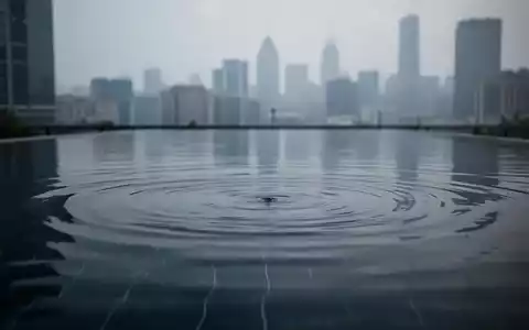 Eine ruhige, spiegelnde Wasseroberfläche mit einer unscharfen Stadtkulisse im Hintergrund, die Stille vor einem Ereignis symbolisiert. - Foto: über boerse-global.de