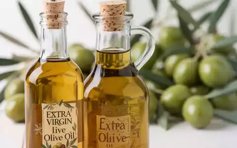 Nahaufnahme einer Glasflasche Olivenöl mit unscharfem Hintergrund aus frischen grünen Oliven und Blättern. - Foto: über boerse-global.de