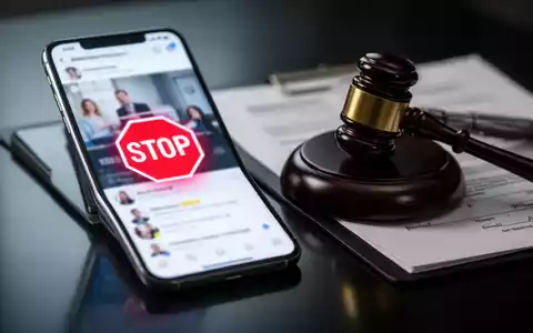 Smartphone-Bildschirm mit rotem 'STOP'-Symbol über unscharfem Social-Media-Feed, Hammer und Rechtsdokumenten auf dunkler Oberfläche. - Foto: über boerse-global.de