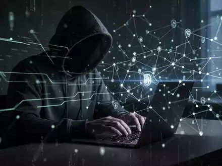 Eine schattenhafte Figur mit Kapuzenpullover tippt auf einem Laptop, umgeben von leuchtenden digitalen Linien und Netzwerkknoten. - Foto: über boerse-global.de