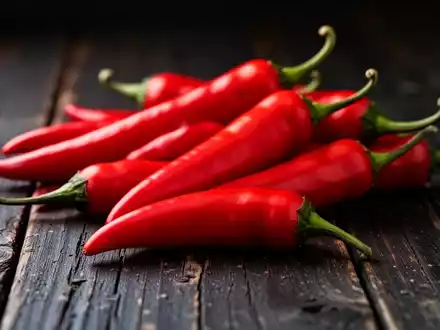 Nahaufnahme von leuchtend roten Chilischoten auf einem rustikalen Holztisch bei stimmungsvoller Beleuchtung. - Foto: über boerse-global.de