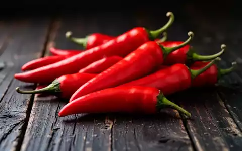 Nahaufnahme von leuchtend roten Chilischoten auf einem rustikalen Holztisch bei stimmungsvoller Beleuchtung. - Foto: über boerse-global.de