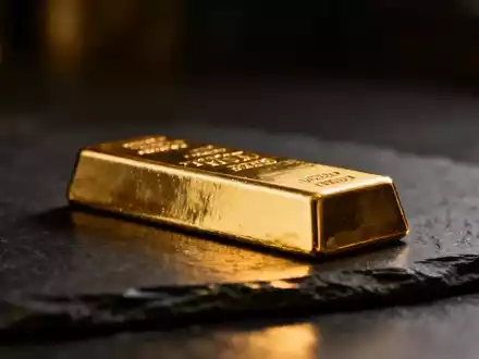 Ein glänzender Goldbarren auf einem dunklen, strukturierten Untergrund bei dramatischem Licht. - Foto: über boerse-global.de