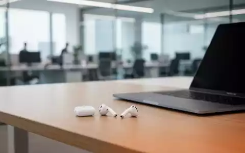 Weiße AirPods 4 Ohrhörer liegen auf einem Holz-Schreibtisch neben einem Laptop. - Foto: über boerse-global.de