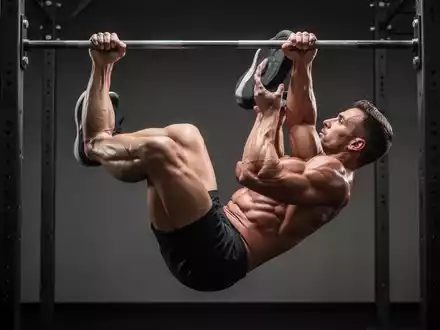 Sportler beim kontrollierten Ausführen von Hanging Leg Raises an einer Klimmzugstange in einem modernen Fitnessstudio. - Foto: über boerse-global.de