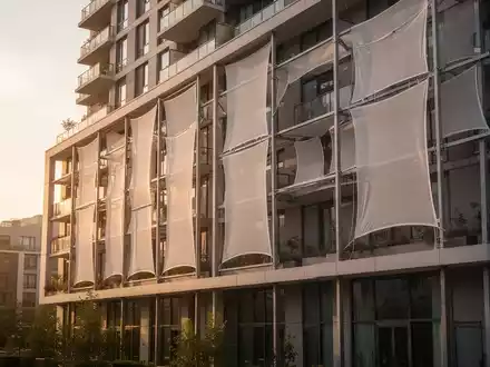 Moderne Wohnhausfassade mit textiler Membrankühlung zur Hitzereduktion an einem sonnigen Tag. - Foto: über boerse-global.de
