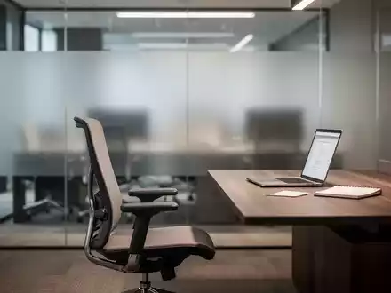Moderner, minimalistischer Büroarbeitsplatz mit einem leeren Schreibtisch und einem ergonomischen Stuhl vor einer Glaswand. - Foto: über boerse-global.de