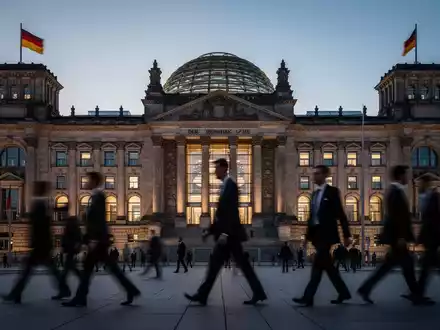 Das Berliner Reichstagsgebäude bei Dämmerung mit den Silhouetten von Politikern im Vordergrund. - Foto: über boerse-global.de