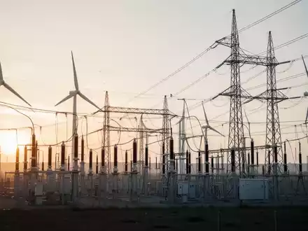 Moderne Hochspannungstrassen und Windkraftanlagen in einer technologisch geprägten Industrielandschaft bei Sonnenaufgang. - Foto: über boerse-global.de
