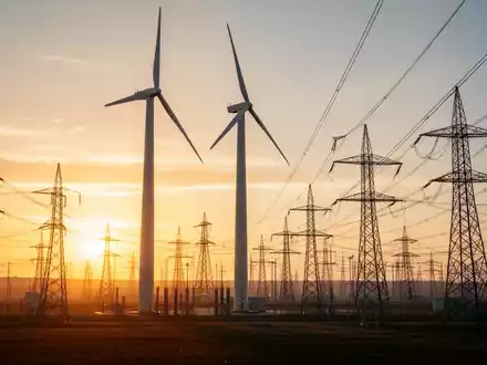 Moderne Windkraftanlage und Stromübertragungsinfrastruktur bei Sonnenuntergang als Symbol für Energieerzeugung. - Foto: über boerse-global.de