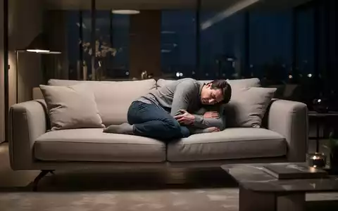 Eine Person schläft in einer unnatürlichen, unbequemen Haltung auf einem Sofa in einem Wohnzimmer. - Foto: über boerse-global.de