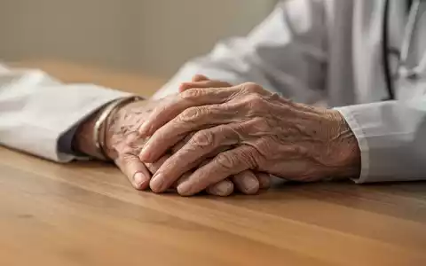 Nahaufnahme der Hände eines älteren Menschen, die auf einem Holztisch ruhen, symbolisch für die Lebenserwartung. - Foto: über boerse-global.de
