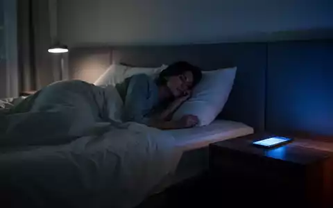 Eine Person liegt nachts in einem abgedunkelten Schlafzimmer, während das Licht eines Smartphones auf den Nachttisch fällt. - Foto: über boerse-global.de