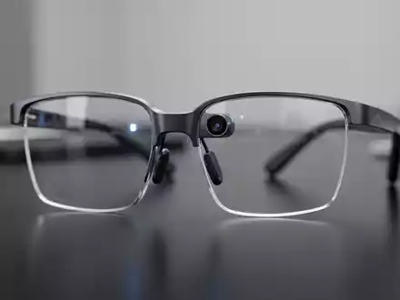Nahaufnahme einer modernen Smart Brille mit sichtbarer Kameralinse auf einem dunklen Schreibtisch. - Foto: über boerse-global.de