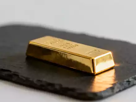 Ein glänzender Goldbarren auf einer dunklen Schieferplatte bei gedimmter, professioneller Beleuchtung. - Foto: über boerse-global.de